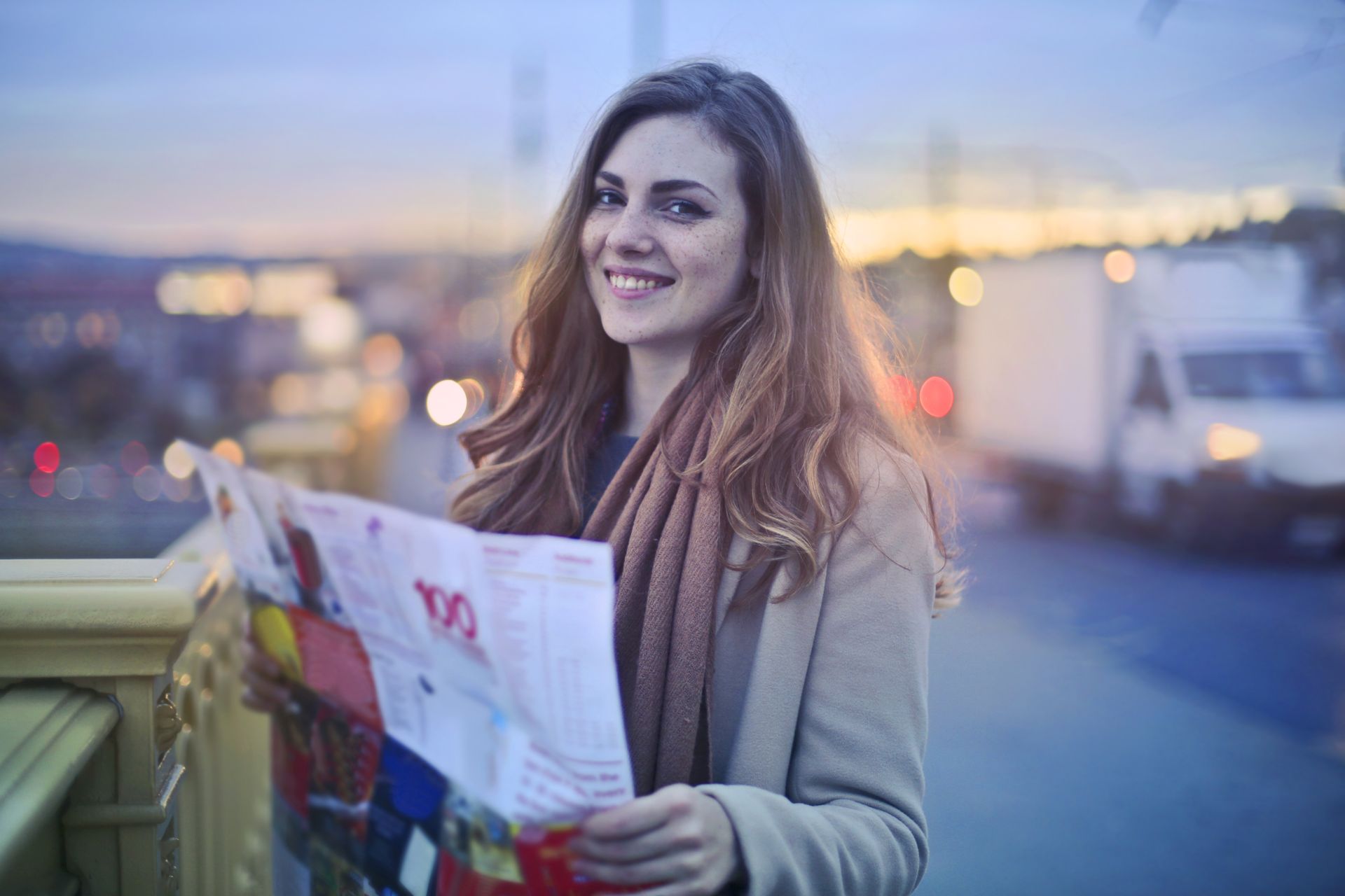 Smiling woman holding a map on a city bridge at twilight, highlighting urban exploration.