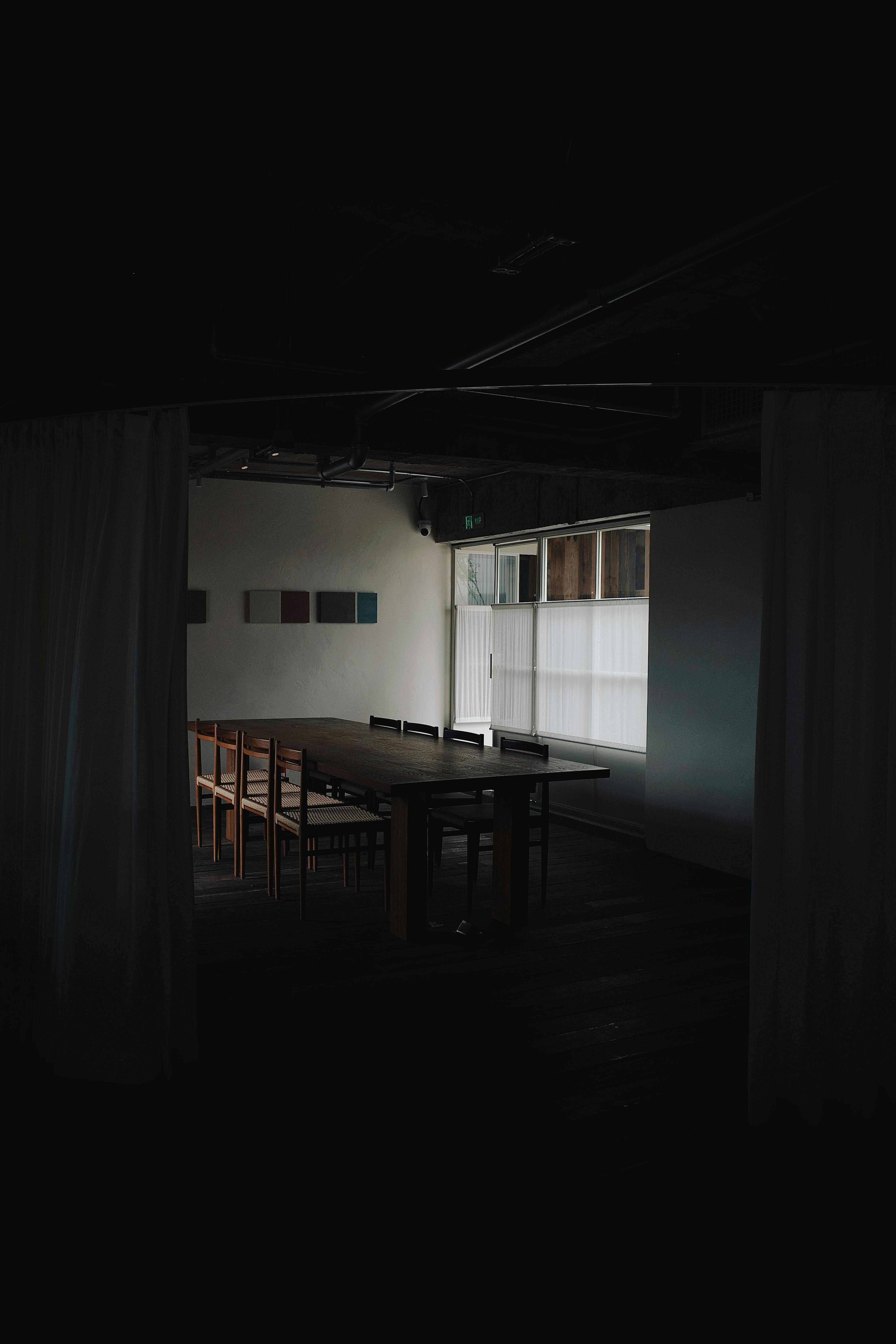 Dark, minimalistic dining room with wooden table and chairs, creating a moody ambiance.