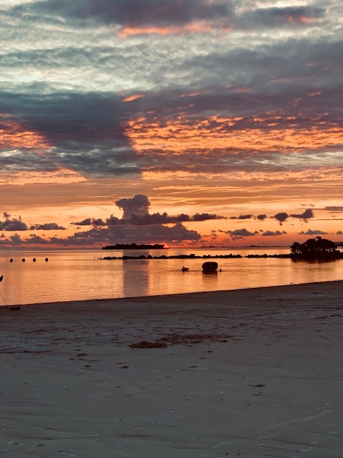 Picturesque scenery of empty sandy beach against cloudy orange sunset sky reflecting on water surface