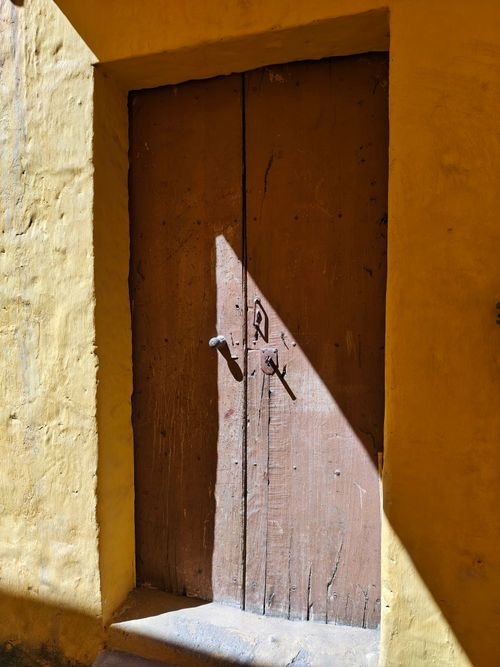 Free A vintage wooden door with sunlight casting angular shadows, set against a yellow wall. Stock Photo
