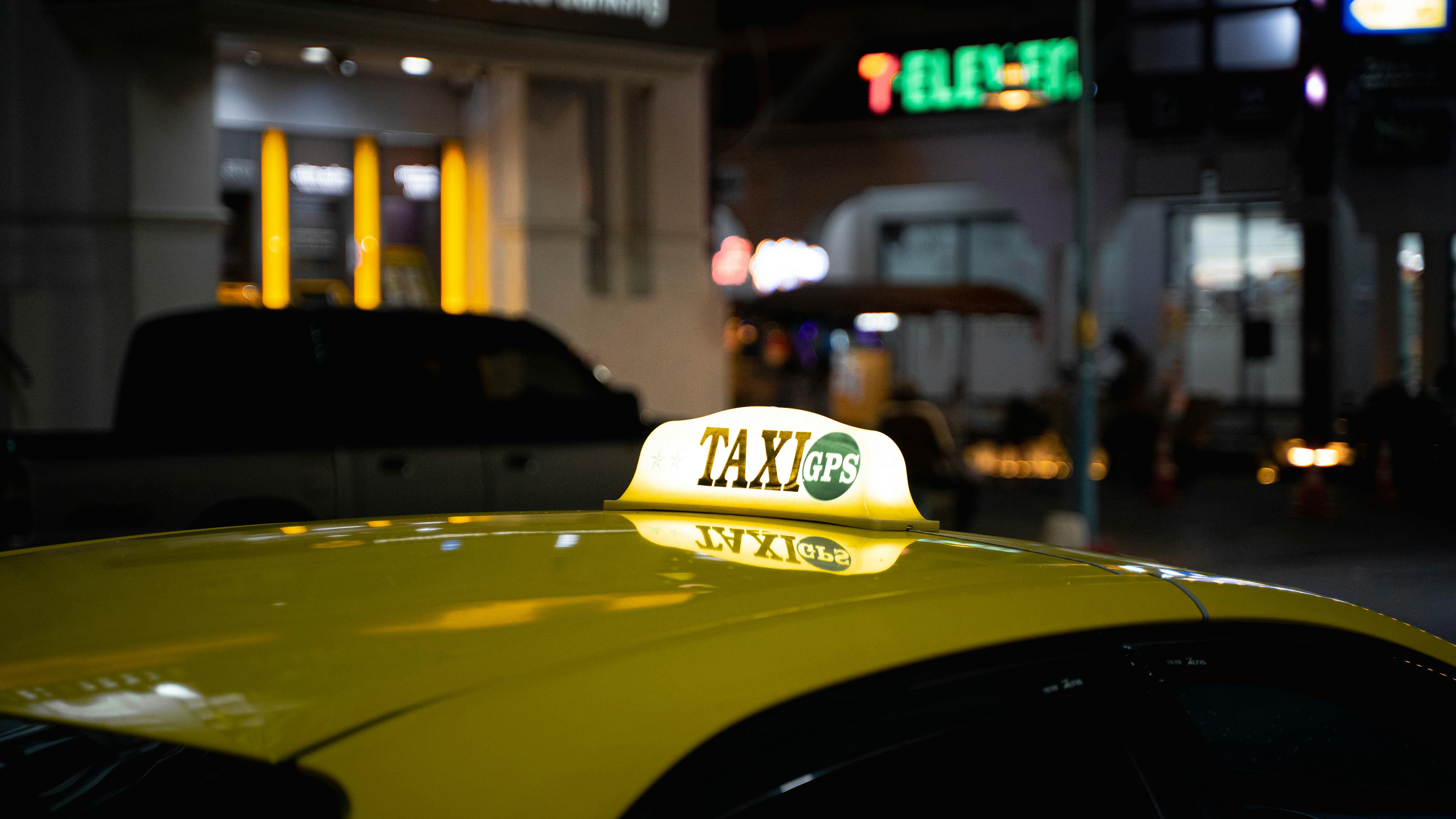 A yellow taxi with a GPS sign captured at night in bustling Thailand.