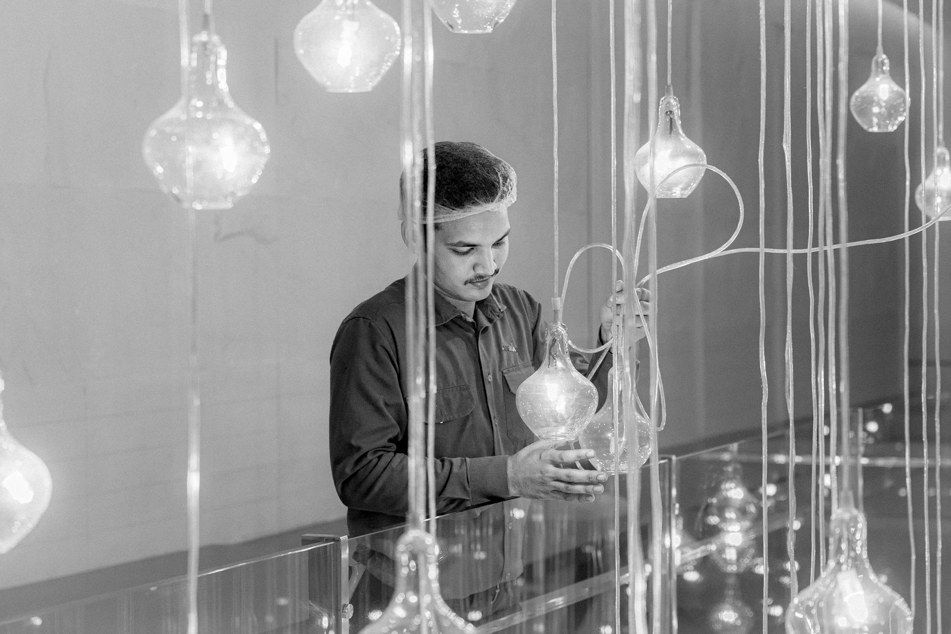 Black and white photo of a man arranging hanging light bulbs indoors, creating a modern aesthetic.