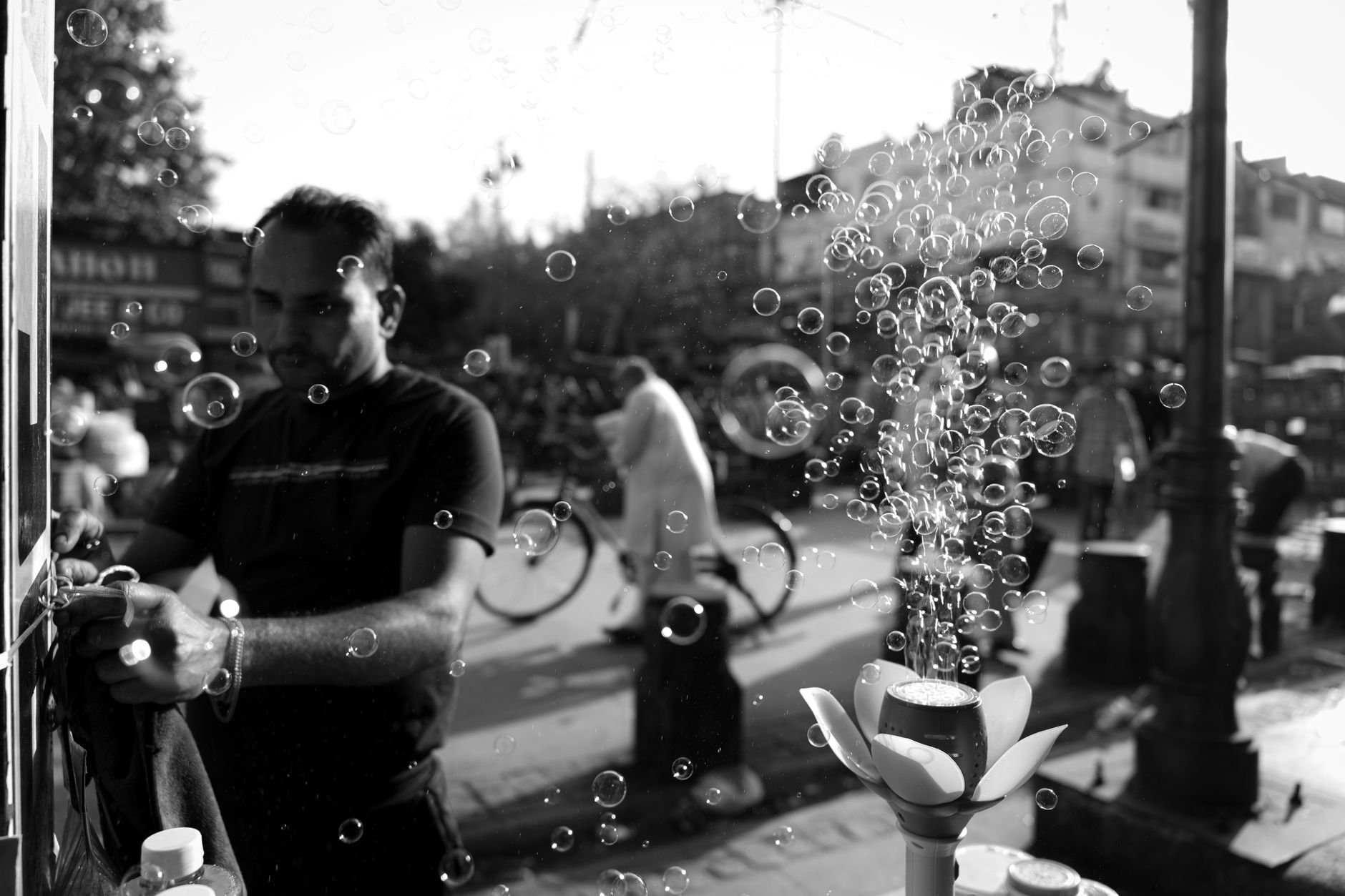 Black and white street photo showing a vendor with bubbles floating around, capturing urban life.