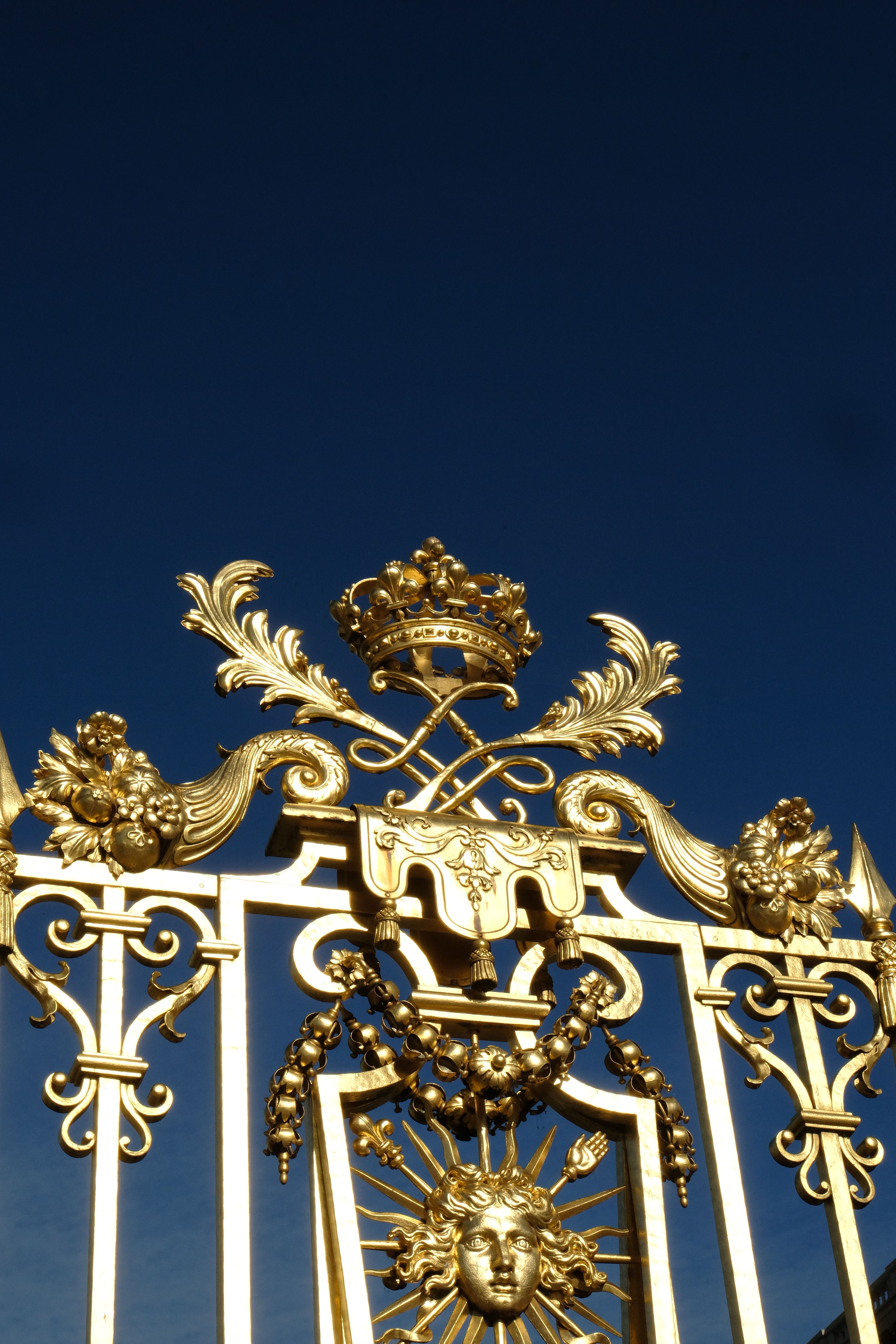 Elegant golden gates at the Palace of Versailles against a clear blue sky.