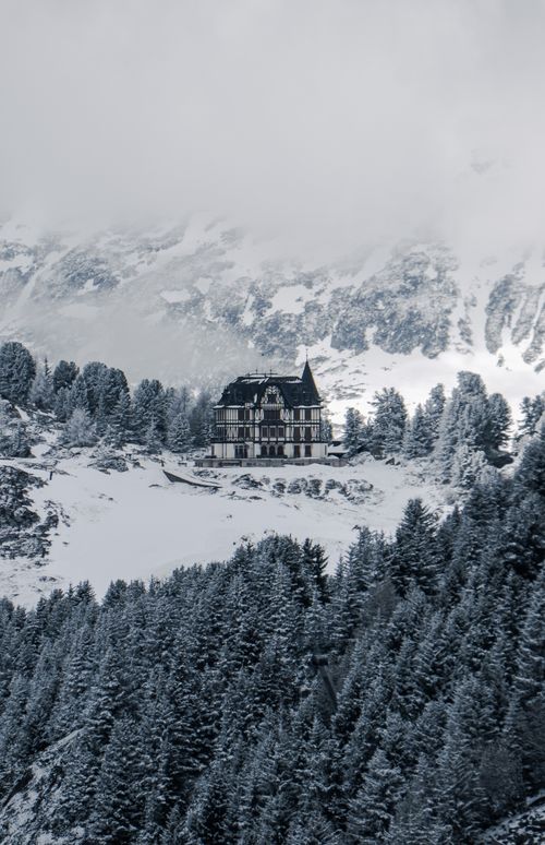 Free A picturesque snowy chalet nestled in the Swiss Alps, framed by frosty pine trees and mountains. Stock Photo