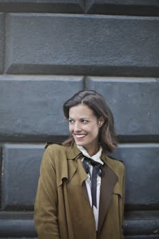 一位穿着棕色外套的优雅女人对着纹理墙壁微笑