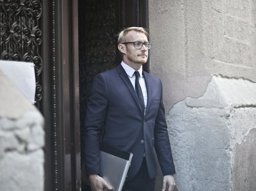 Photo of Man in Blue Suit Jacket and Eyeglasses Standing in Doorway carrying a Laptop