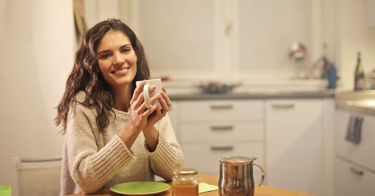 Woman smiling while holding a cup of tea in a cozy kitchen setting.
