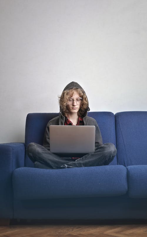 Free Photo of Person Sitting on Blue Couch Using a Laptop Stock Photo