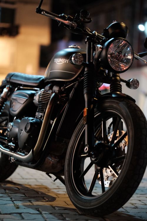 Free Stylish Triumph motorcycle parked outdoors at night on cobblestone street. Stock Photo