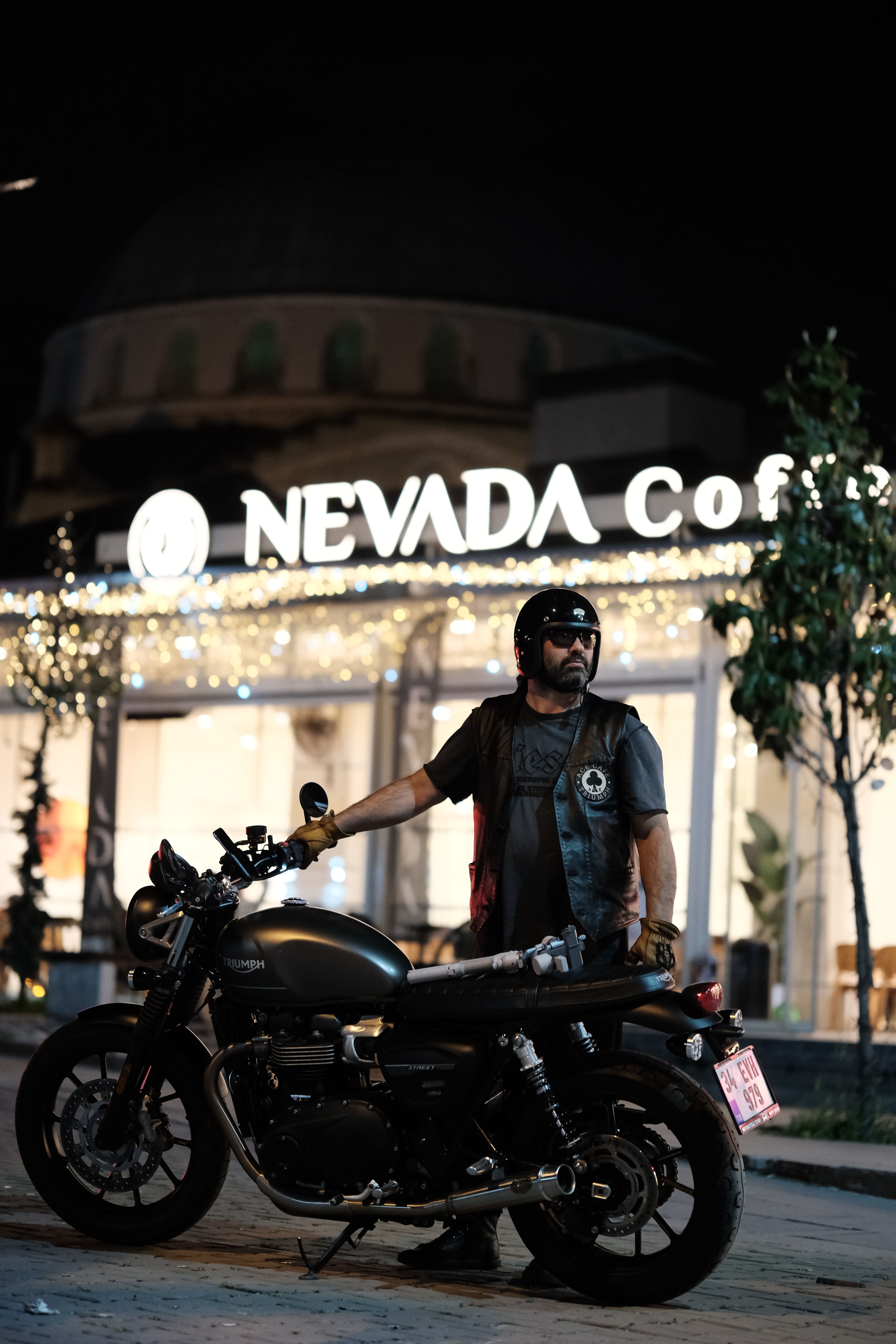 A biker poses with a motorcycle outside the illuminated Nevada Cafe during nighttime.