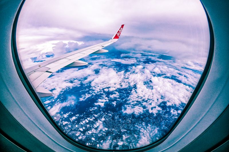 Wide angle of rocky ground through cloudy sky and plane wing from window of aircraft