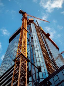 A towering skyscraper under construction in Wrocław, Poland with cranes and blue sky.