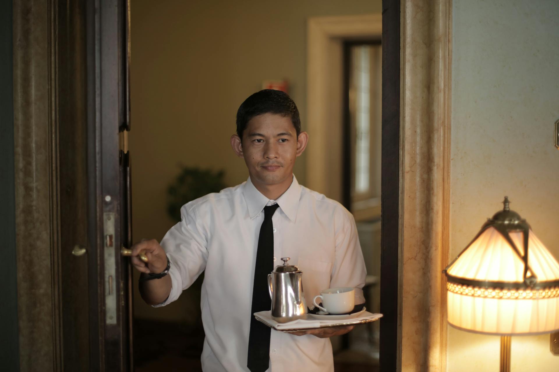 Smiling waiter serves coffee in a hotel room, offering hospitality and service.