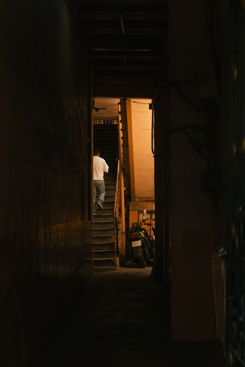 Free A dimly lit urban alleyway featuring a person climbing stairs, creating a mysterious atmosphere. Stock Photo
