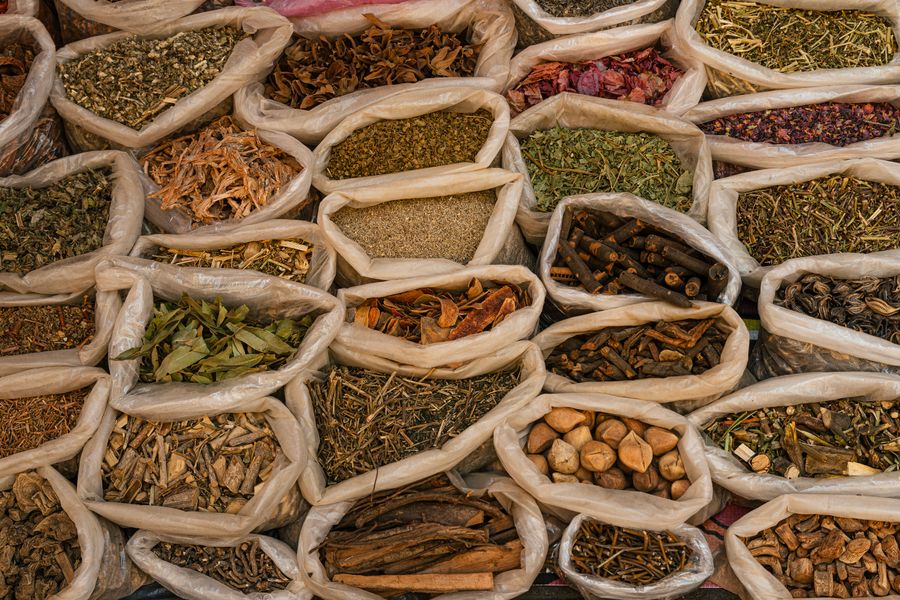 Bags filled with various dried herbs and spices displayed in a traditional market setting.