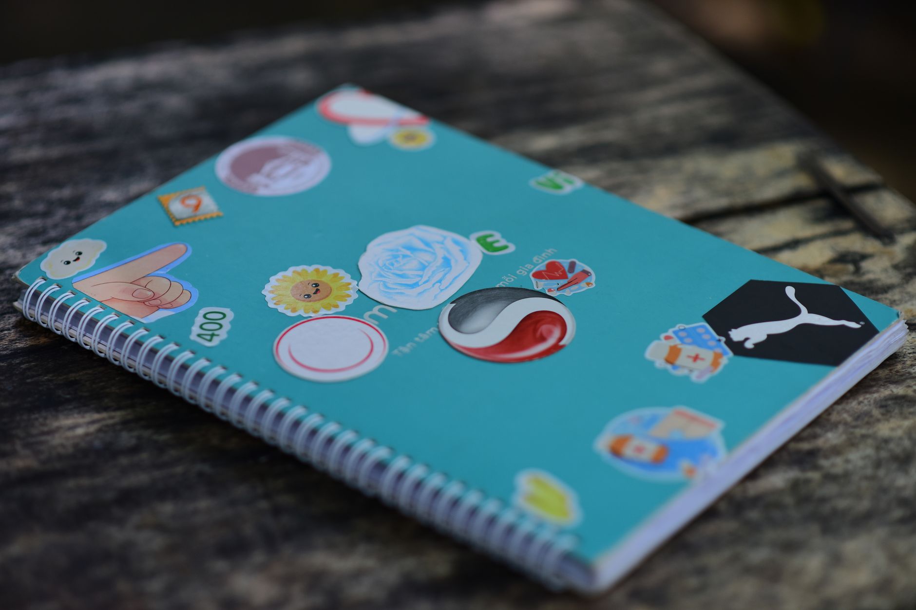 A blue spiral notebook adorned with colorful stickers on a rustic wooden surface.