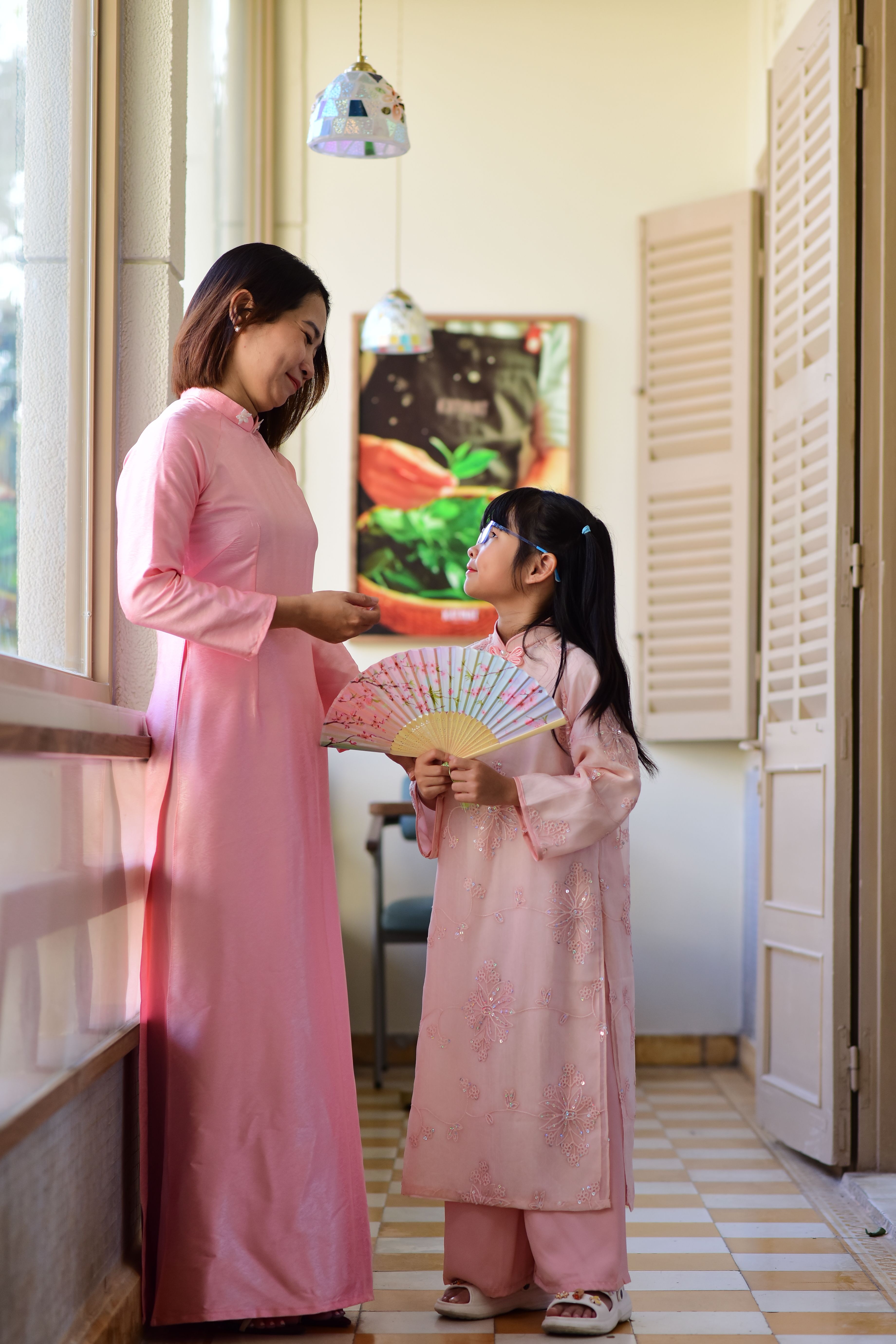 A mother and daughter share a moment in traditional pink Ao Dai dresses indoors.
