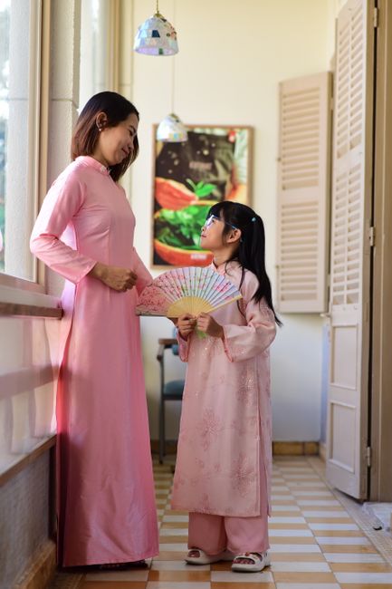 A woman and young girl in pink traditional clothing indoors share a loving moment.