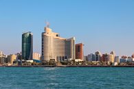 A panoramic view of Kuwait City's modern skyline with waterfront under clear blue skies.