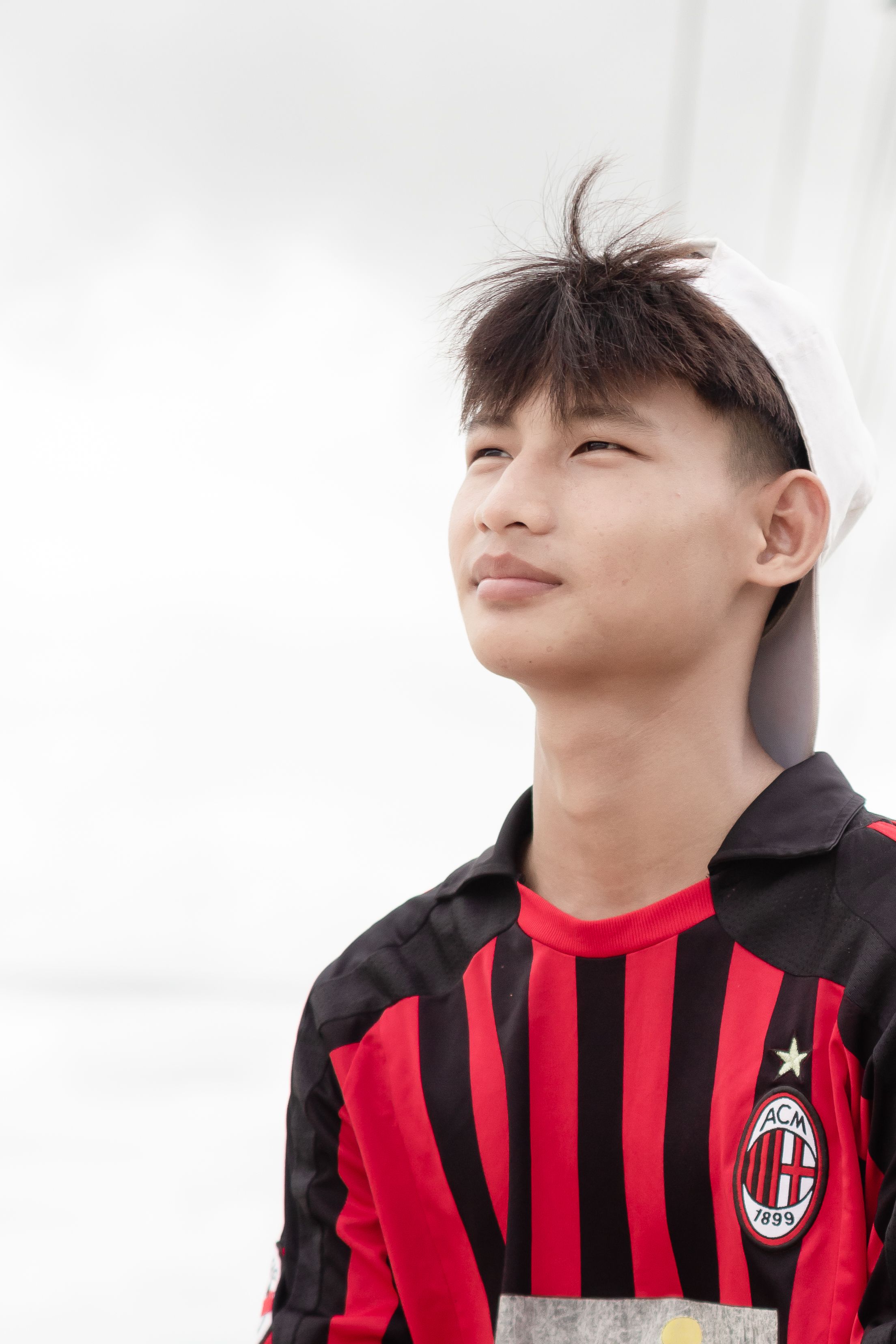 Portrait of a young man wearing a red and black football jersey, gazing into the distance.