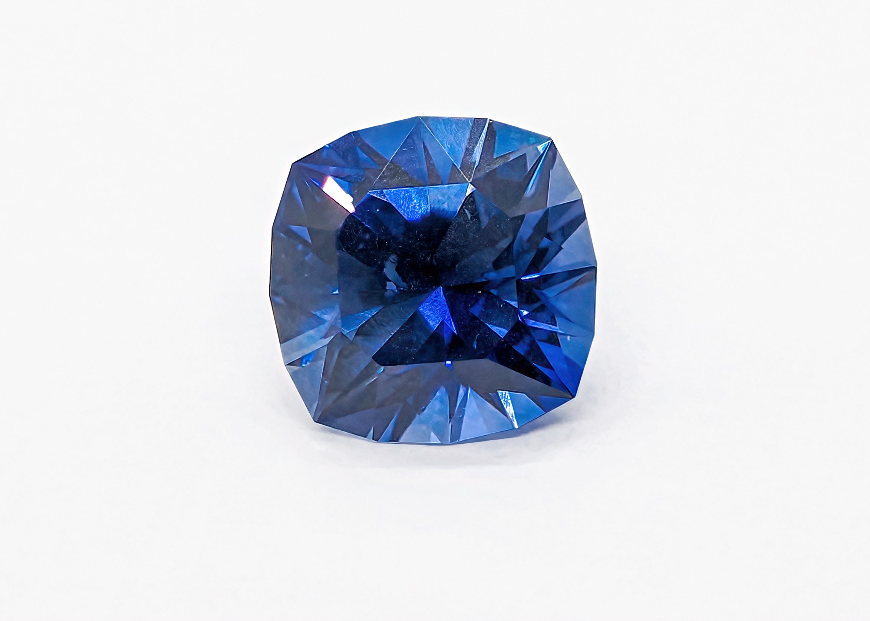 Close-up of a faceted deep blue gemstone catching light, showing bright reflections across its facets