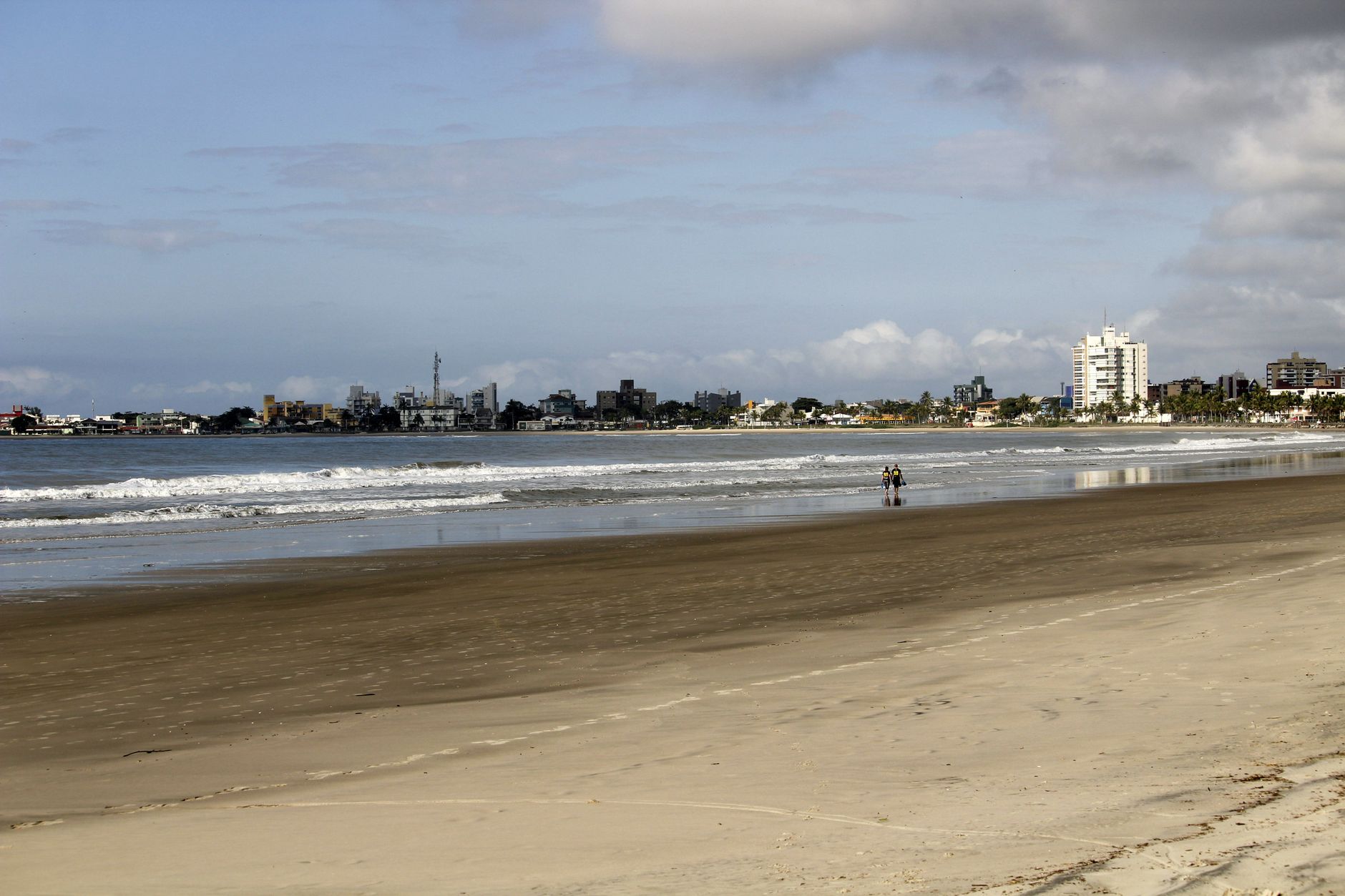 A wide sandy beach with distant city skyline and gentle ocean waves under a bright sky.