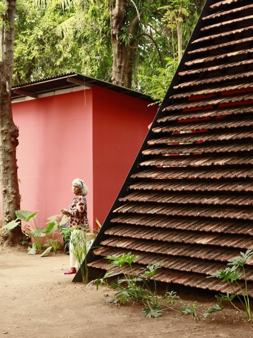 Free Elderly woman stands by modern red structure in lush garden setting. Stock Photo