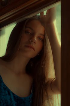 一位体贴的年轻女子沐浴在柔和的自然光线中，透过窗户凝视着