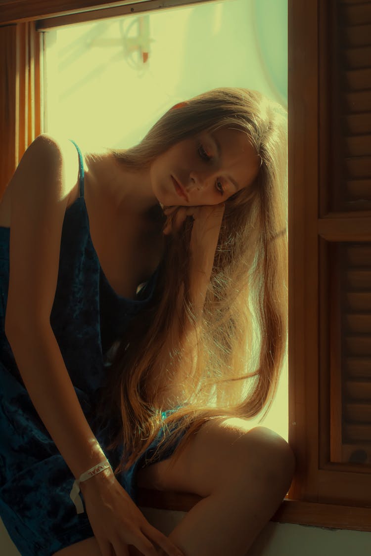 Photo Of Bored Woman In Blue Sleeveless Dress Sitting On Window