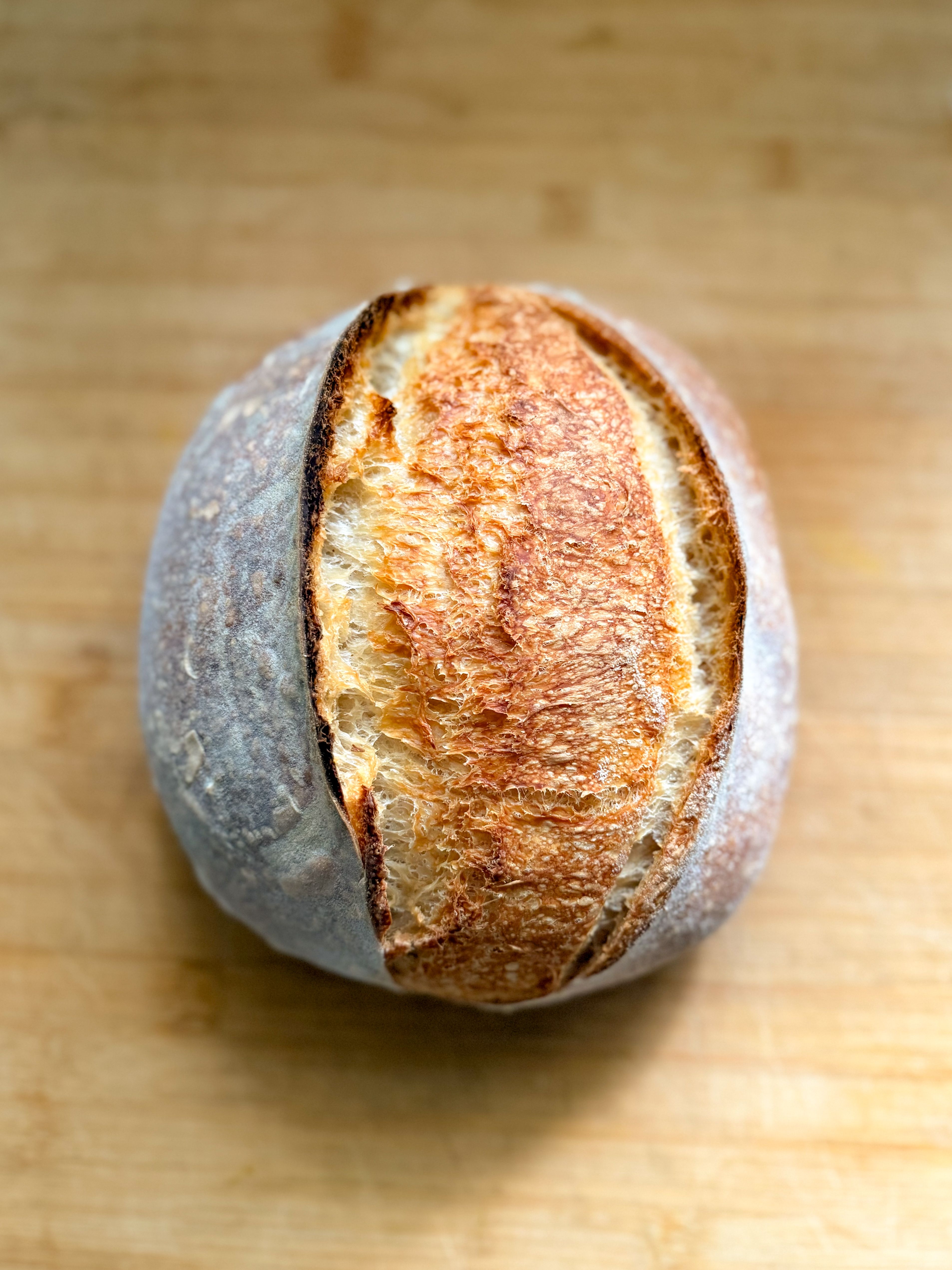 Top view of a beautifully baked artisan round bread on a wooden surface.