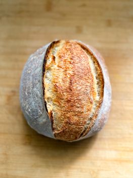 Top view of a beautifully baked artisan round bread on a wooden surface.