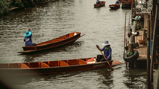 Traditional wooden boats navigate a canal in Bangkok, showcasing local culture and lifestyle.
