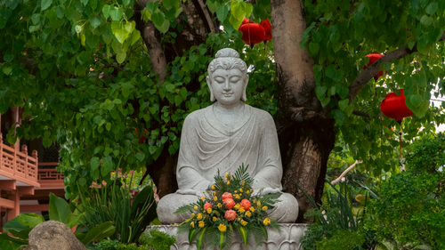 Free Tranquil Buddha statue surrounded by lush greenery and colorful flowers outdoors. Stock Photo