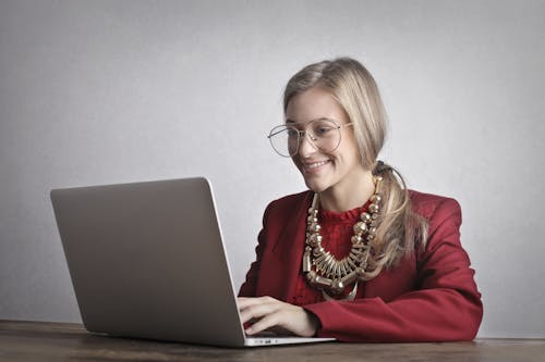 Foto De Mujer Sonriente Con Un Abrigo Rojo Y Gafas Usando Una Computadora Portátil