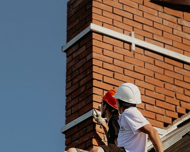 Chimney repair on a roof Two roofers in hard hats repairing a chimney on a house roof
