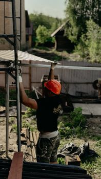 A construction worker in a hard hat and gloves installs a roofing panel on a sunny day.