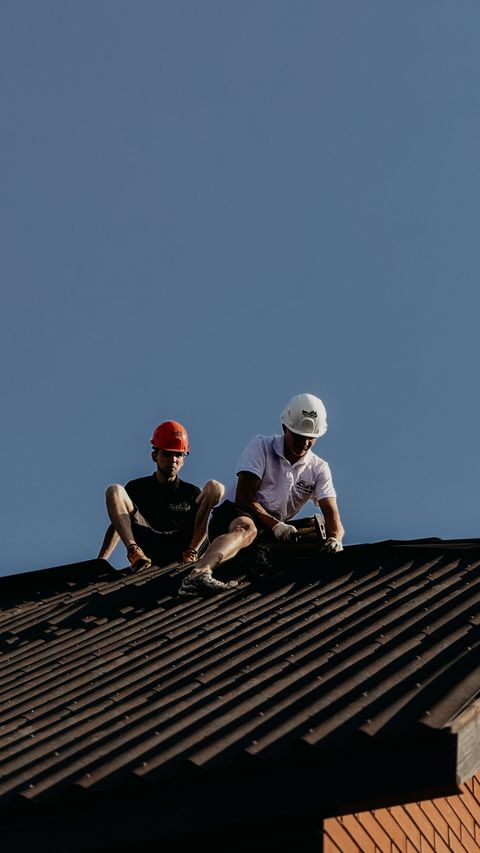 Two roofers repairing a roof under a blue sky