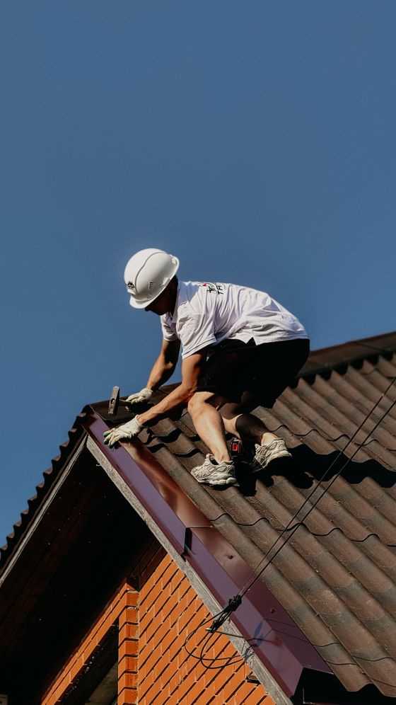 Roofer in a safety helmet renovating a brick house roof