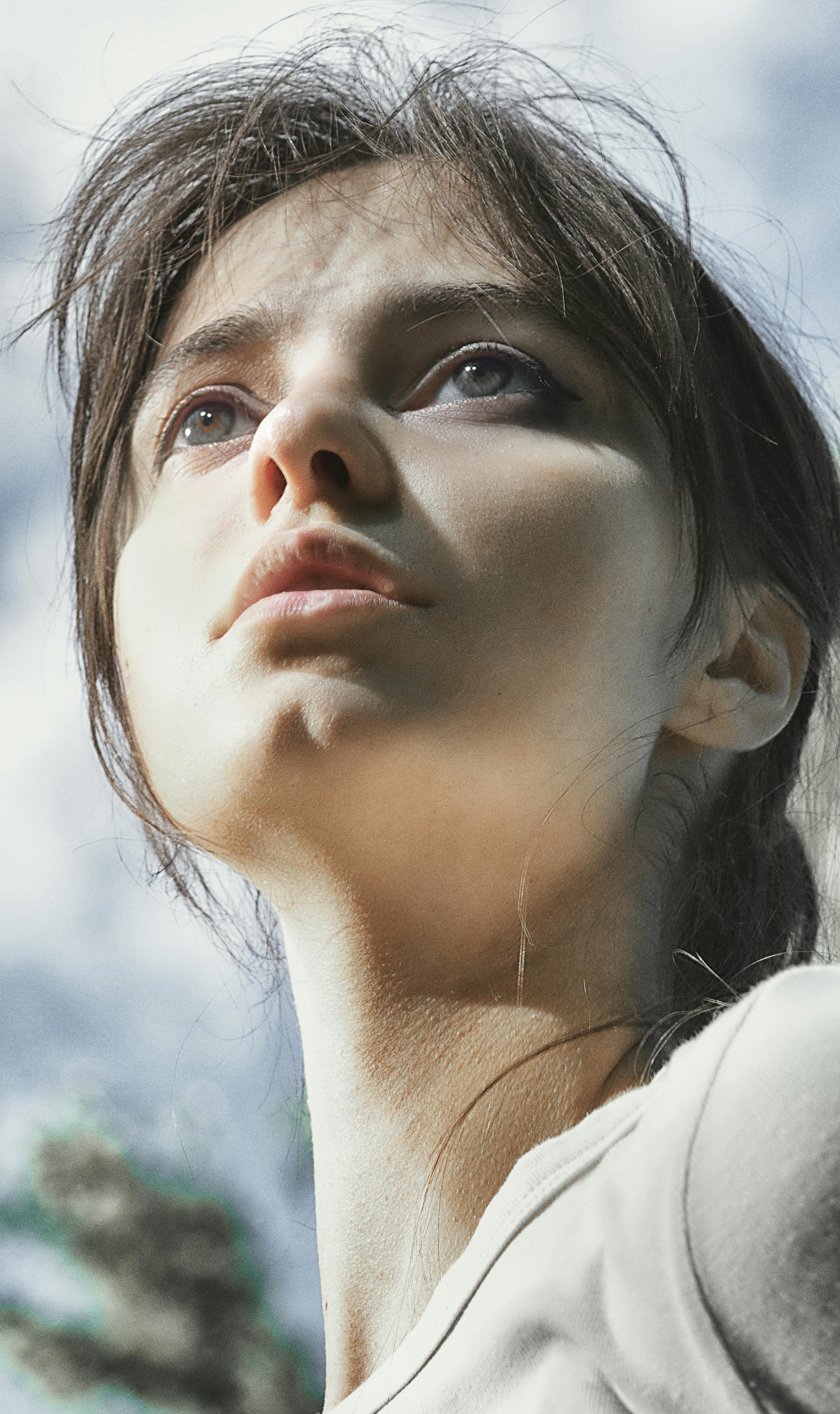 Close-up of a thoughtful young woman looking upward against a blue sky backdrop.