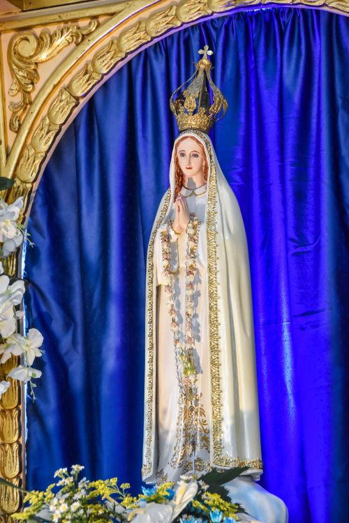 Free A well-lit statue of Our Lady of Fatima with a crown, surrounded by flowers in Baliwag, Philippines. Stock Photo