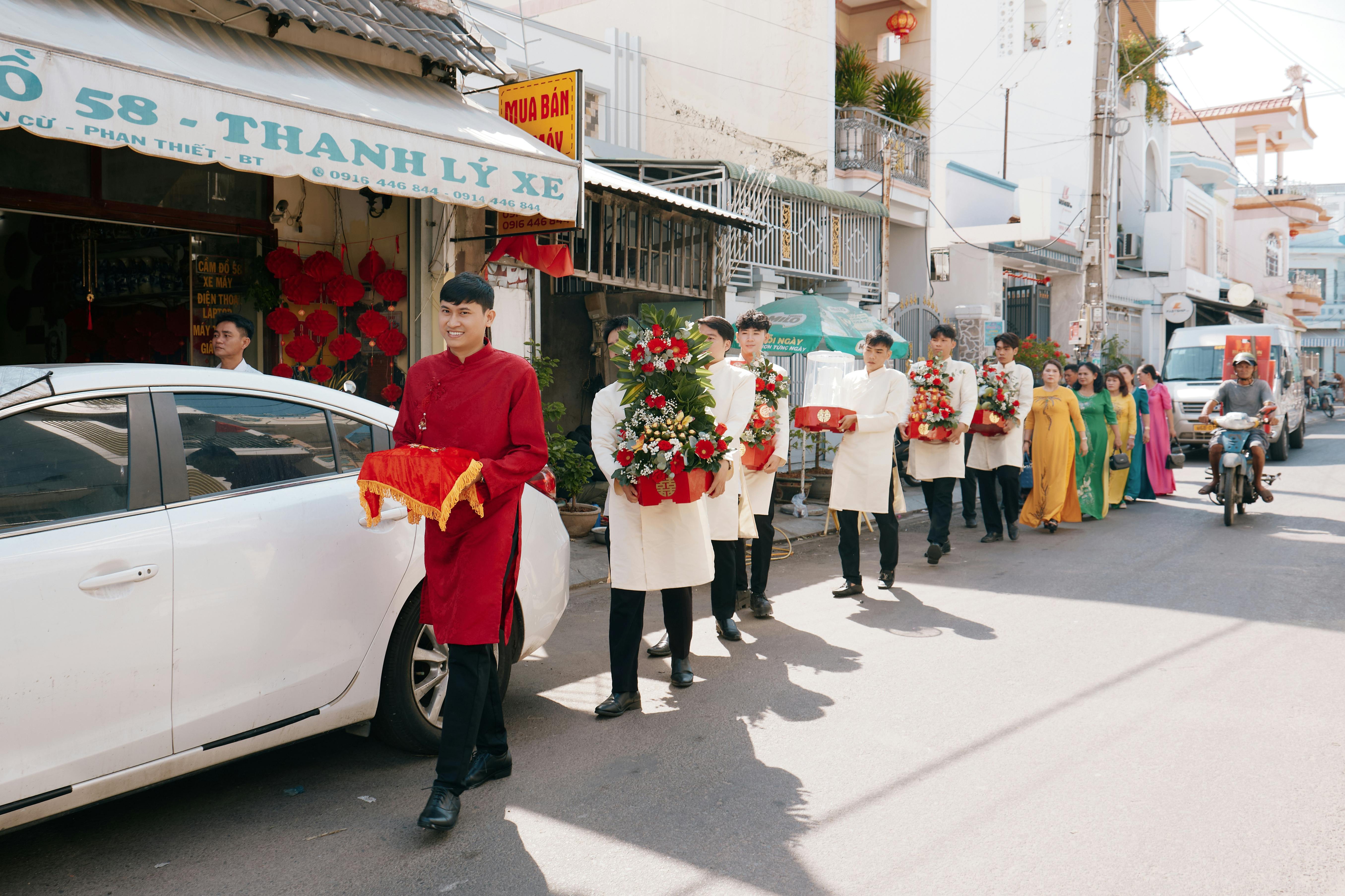 Vietnamese wedding procession with traditional attire and decorations on a sunny day.