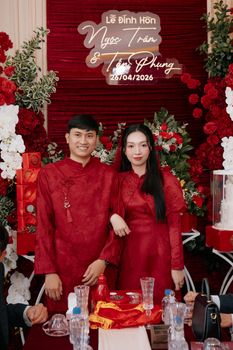 Couple in red outfits during Vietnamese engagement with floral backdrop.