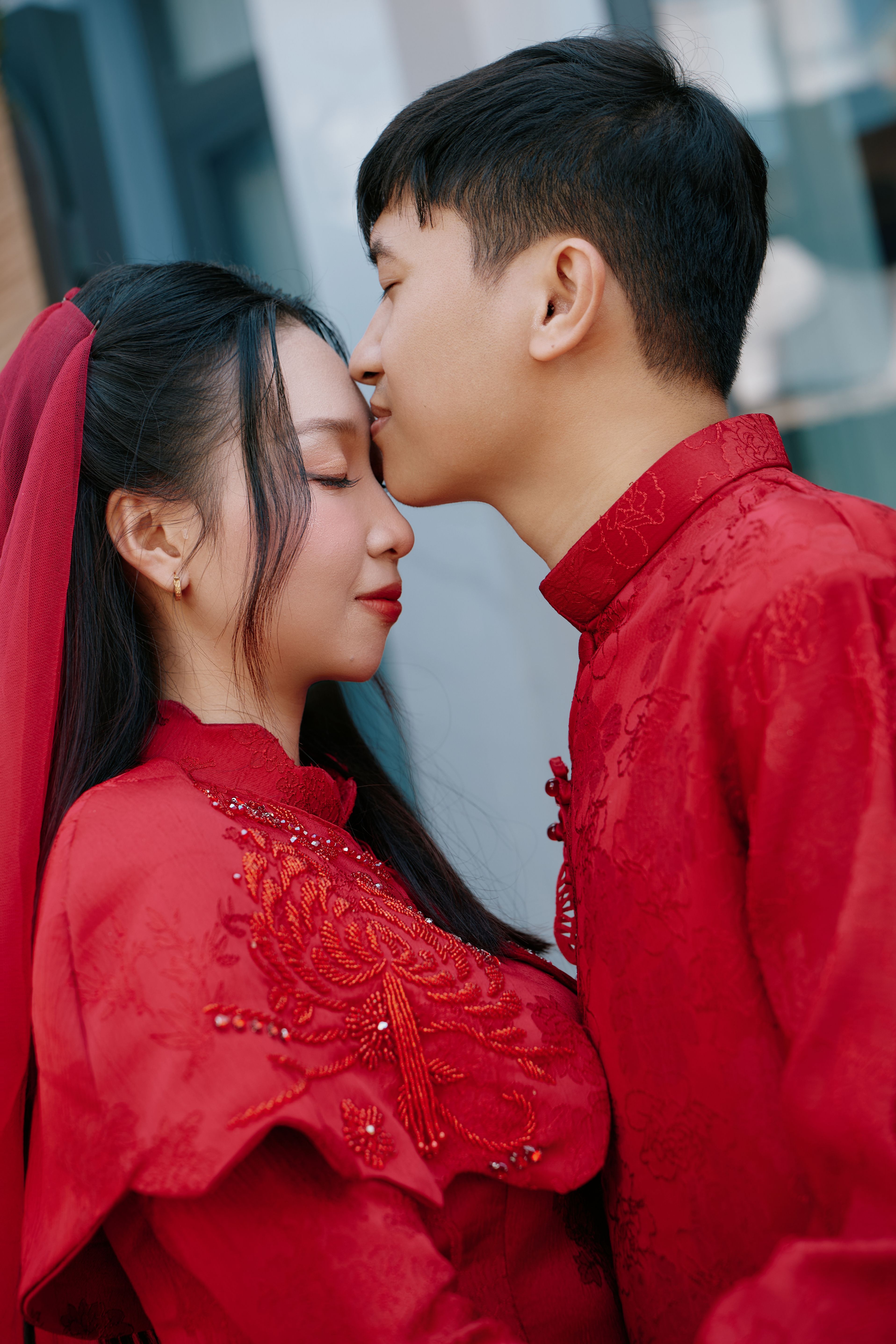 A couple dressed in matching red traditional outfits share an affectionate moment.