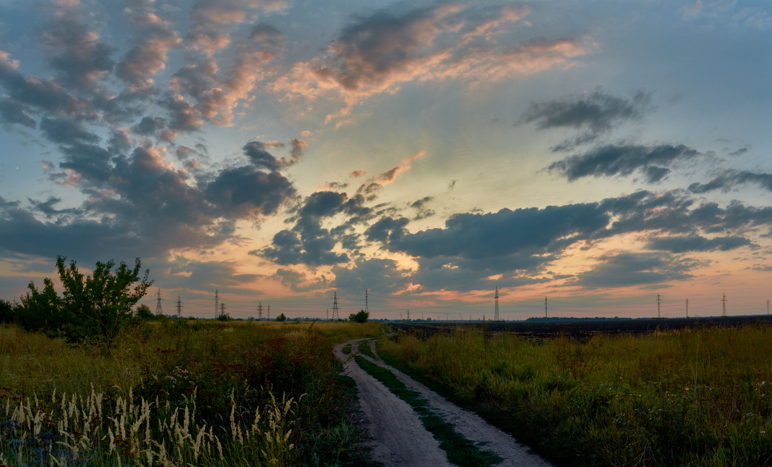 Panoramic view of a country road through a grassy field with a colorful sunset sky.