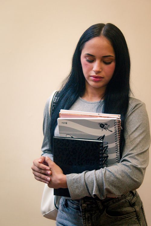 Free Young woman with notebooks standing indoors, representing student life and education. Stock Photo