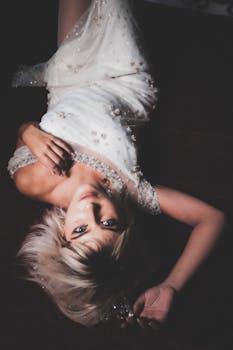 Stylish woman in an elegant white gown poses upside down with a captivating expression.