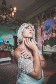 Sensual blond woman wearing white dress with bare shoulders and crystal headdress touching neck sensually
