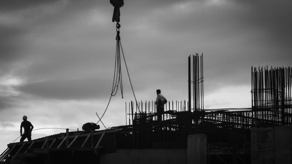 Imagen en blanco y negro de obreros de la construcción en una obra en Estambul, recortados contra un cielo nublado.