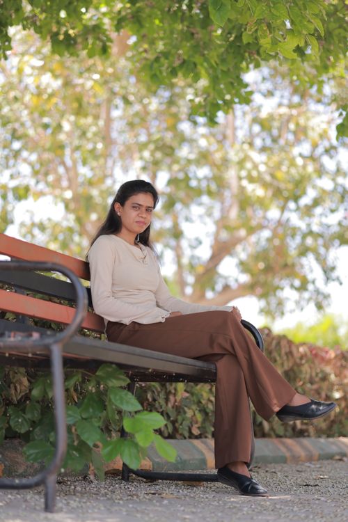 Free A young woman sitting on a park bench under a tree, enjoying a sunny day. Stock Photo